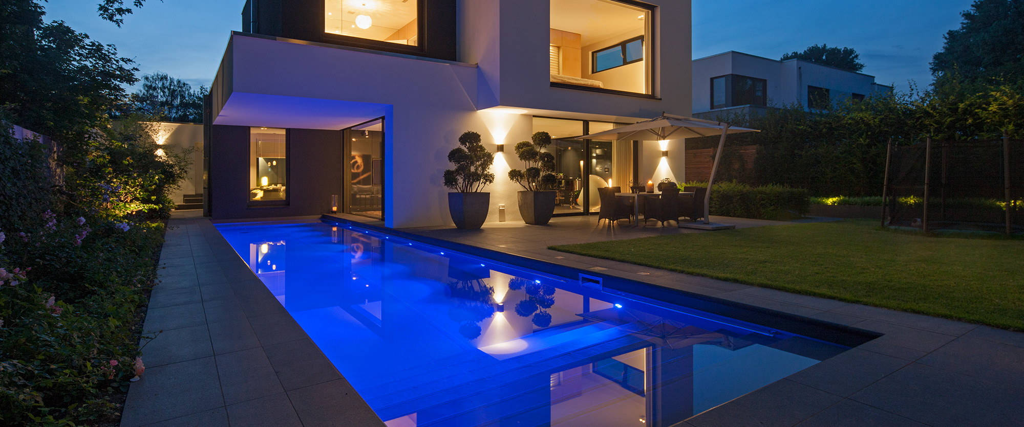 Outdoor pool illuminated blue with back yard and terrace