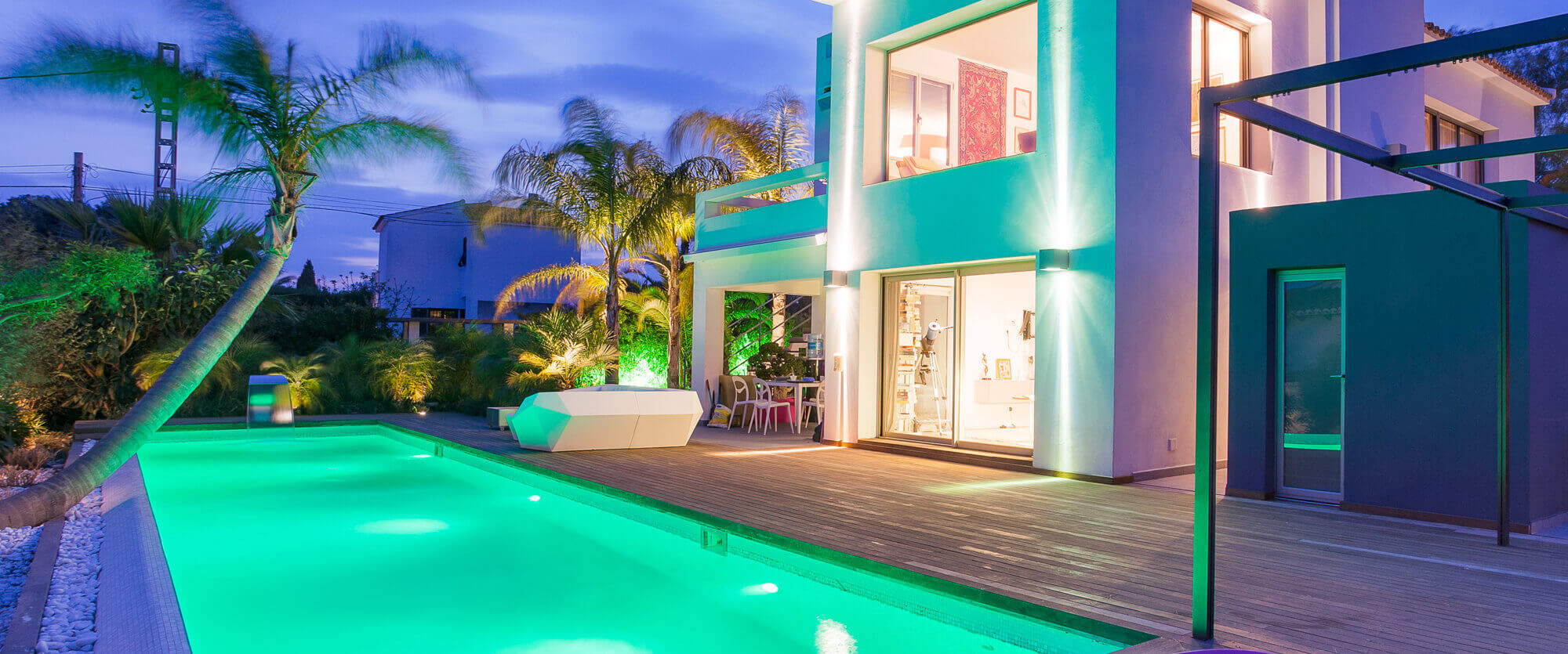 Turquoise-illuminated outdoor pool with illuminated house